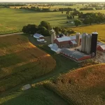 An areal view of a farm with red barn, silos, and corn fields.