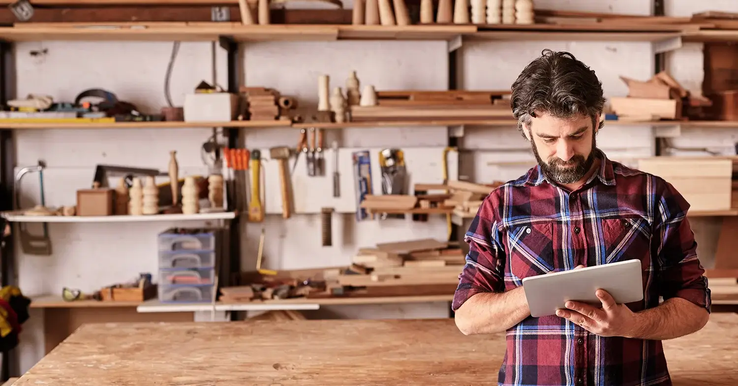 An artisan in a woodshop studio holding a tablet.