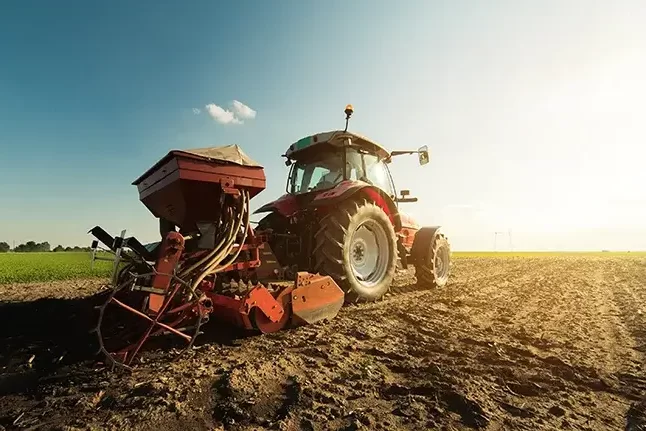 A farmer in a tractor seeing crops in a plowed field.