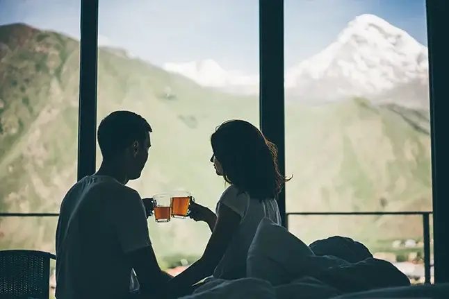 A happy couple drinking tea by a mountain landscape indoors.