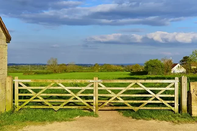 A scenic view of a farm gateway going into a green meadow with a white house in the distance.