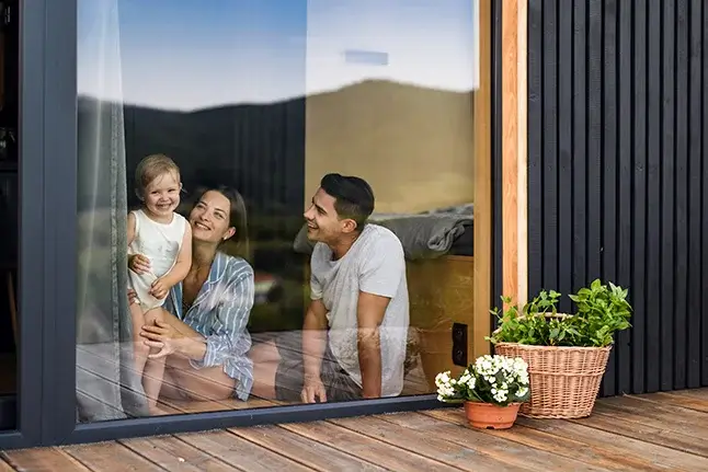 A young couple sits in front of a glass window with their young child.